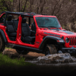 2023 Red Jeep Wrangler driving through water with doors and top off