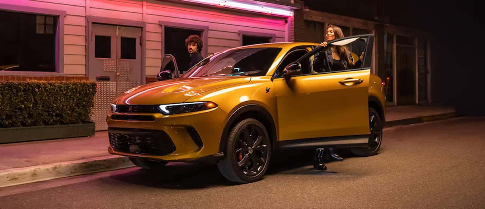 Two people getting out of a 2025 Dodge Hornet SUV parked on a nighttime street