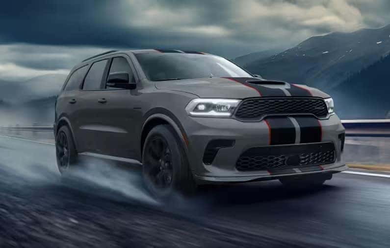 A gray 2026 Dodge Durango SUV driving down a rainy highway with mountains in the background
