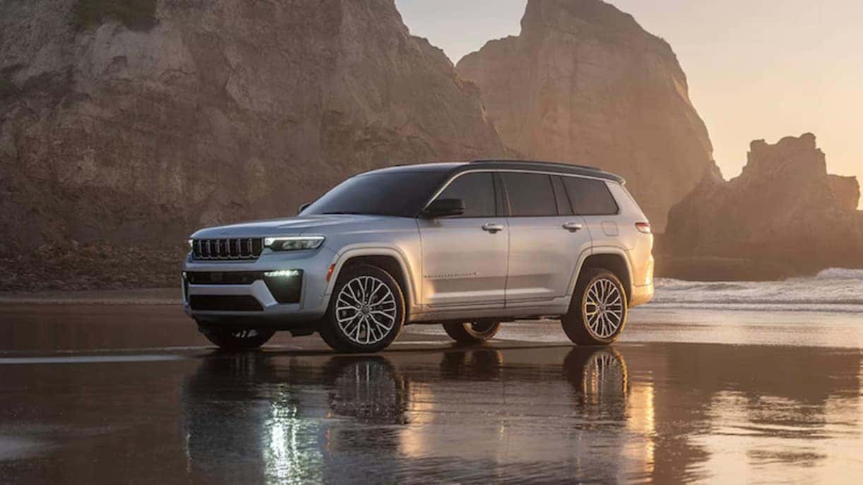 A silver 2026 Jeep Grand Cherokee SUV parked on a beach at dawn