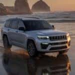 A gray 2026 Jeep Grand Cherokee SUV driving down a beach at sunset