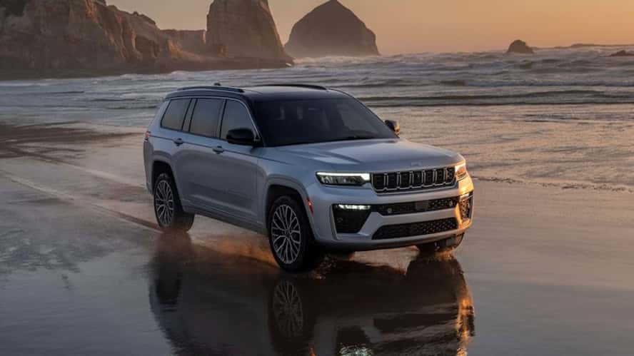 A gray 2026 Jeep Grand Cherokee SUV driving down a beach at sunset