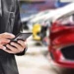 A person in a black suit looking at a cell phone inside a car dealership