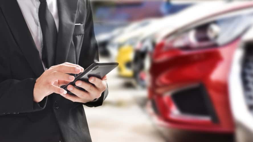 A person in a black suit looking at a cell phone inside a car dealership
