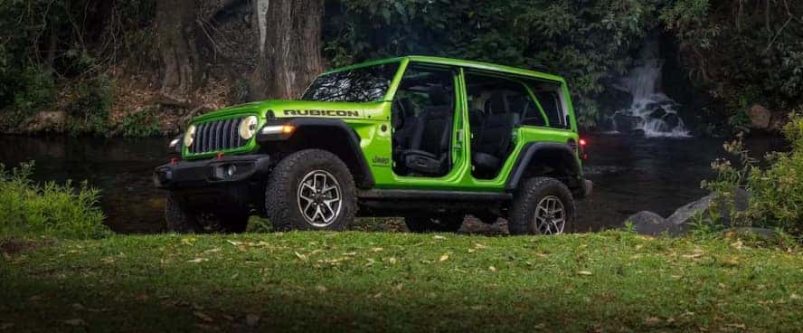 A green Jeep Wrangler parked beside a river