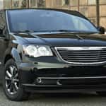 Black Chrysler Town & Country minivan parked in front of an industrial-style glass building, showcasing its sleek design and chrome accents.