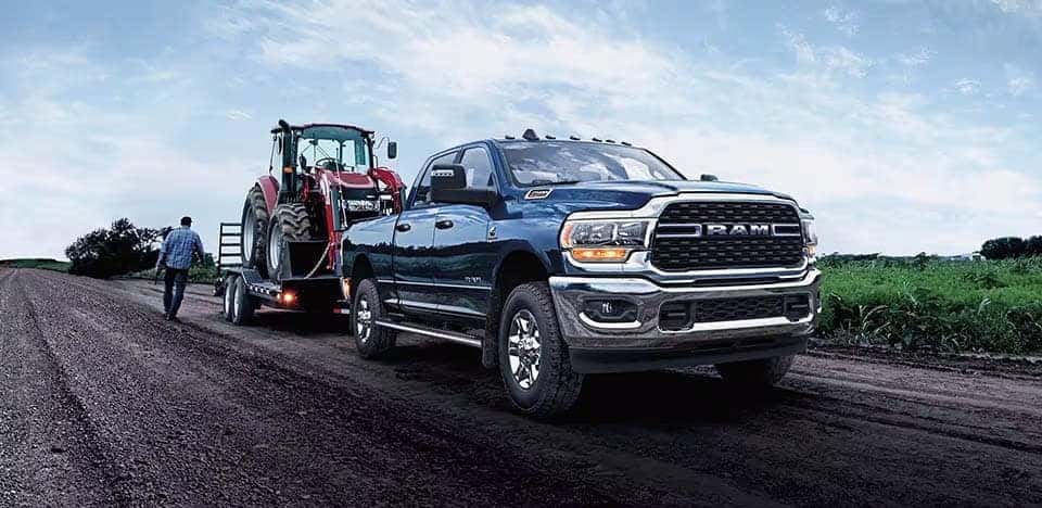 Dodge Ram 2500 Blue pulling construction equipment on dirt road.