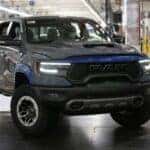 2025 RAM 1500 TRX in gray with blue trim on an assembly line, showcasing aggressive front grille, LED headlights, and off-road tires
