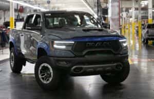 2025 RAM 1500 TRX in gray with blue trim on an assembly line, showcasing aggressive front grille, LED headlights, and off-road tires
