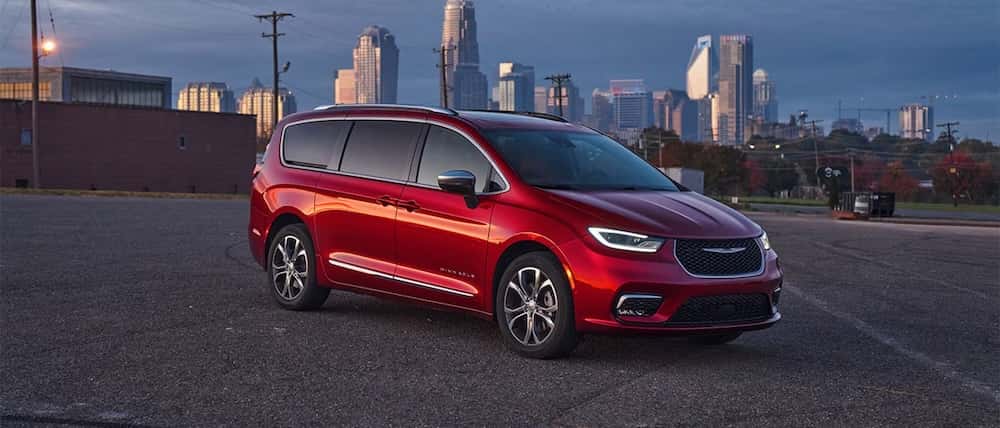sideview of red chrysler pacifica van parked with city skyscape in background