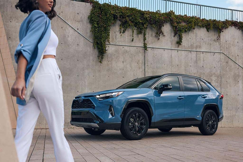 2024 Toyota RAV4 Hybrid in blue parked with a woman walking towards it