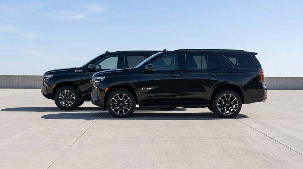 Two full-size Chevrolet SUVs parked side by side showing the size difference in profile