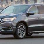 Gray-black 2020 Acura MDX side view with body of water and city skyline background