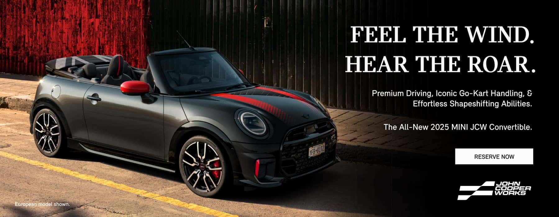 ¾ right view of a black MINI JCW convertible with red stripes on a city street.