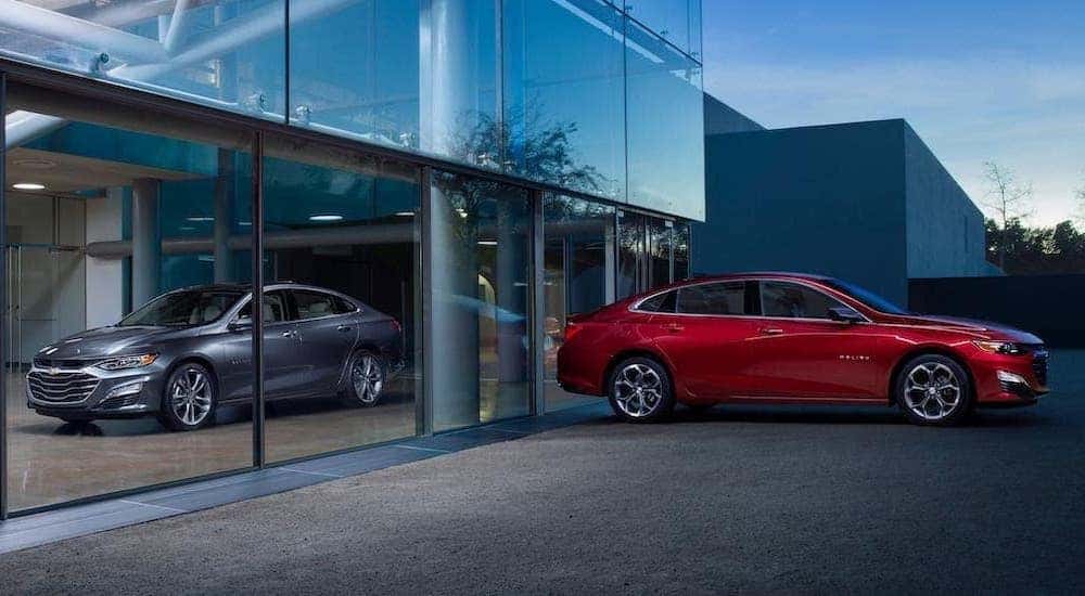 A gray and a red 2020 Chevy Malibu are parked outside a Chevy dealer in Suffolk, VA.
