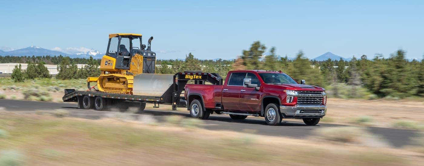 A red 2021 Chevy Silverado 3500HD diesel is towing construction equipment on a highway.