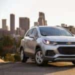 A silver 2021 Chevy Trax is parked on a hill with a city skyline in the background.