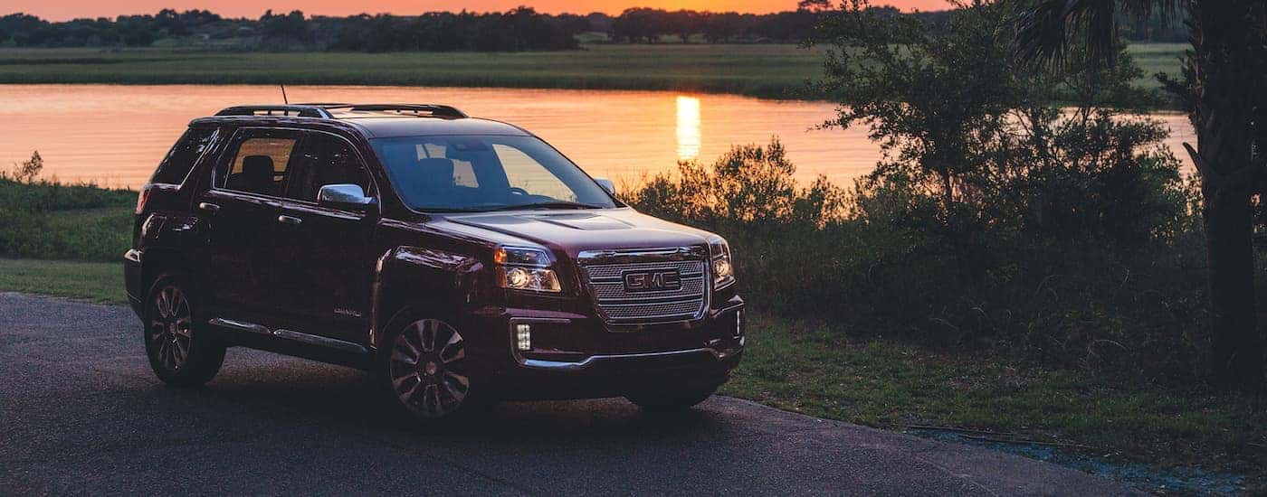 A red 2017 GMC Terrain Denali is shown parked next to a lake at sunset.