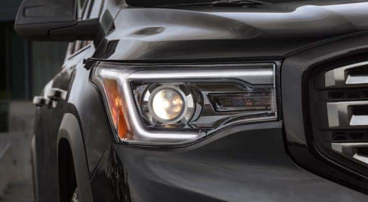 A close up shows the passenger side headlight on a black 2019 GMC Acadia All Terrain.