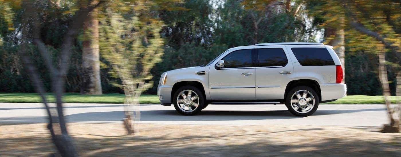 A silver 2011 Cadillac Escalade is shown from the side driving on an open road.