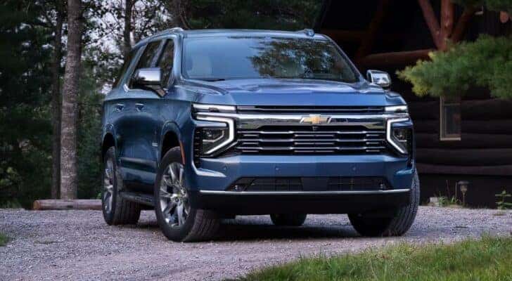 A blue 2025 Chevy Tahoe for sale parked outside a rustic cabin.