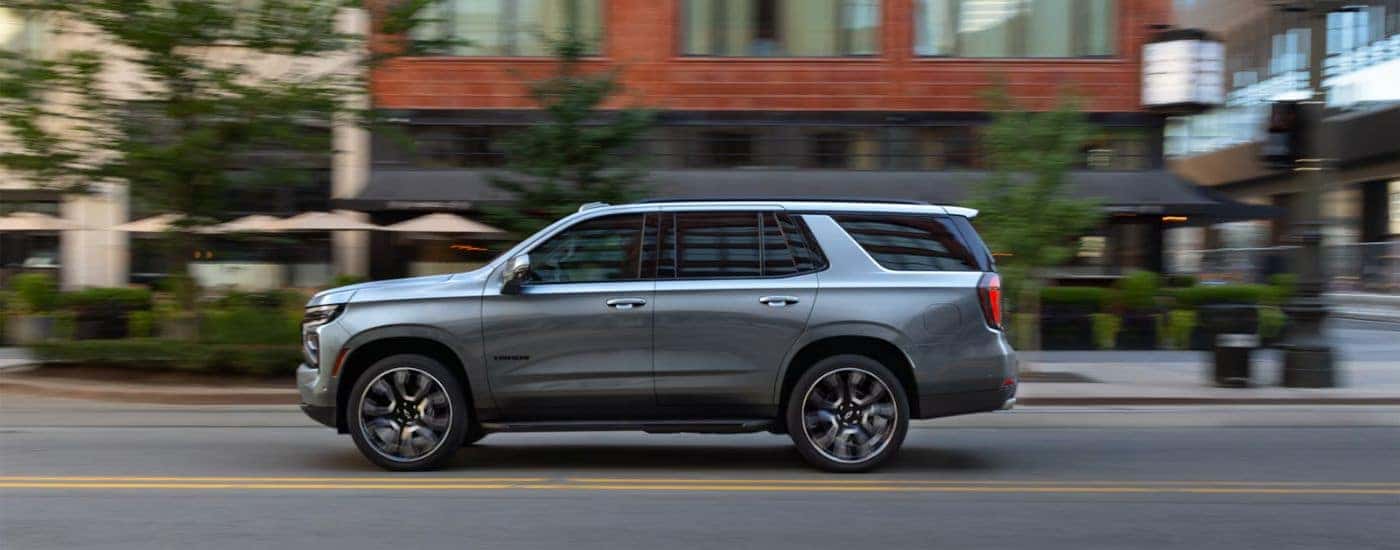 Side view of a silver 2025 Chevy Tahoe driving through blurred city streets.