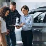Young couple reviewing the terms of their car loan with a dealership representative.