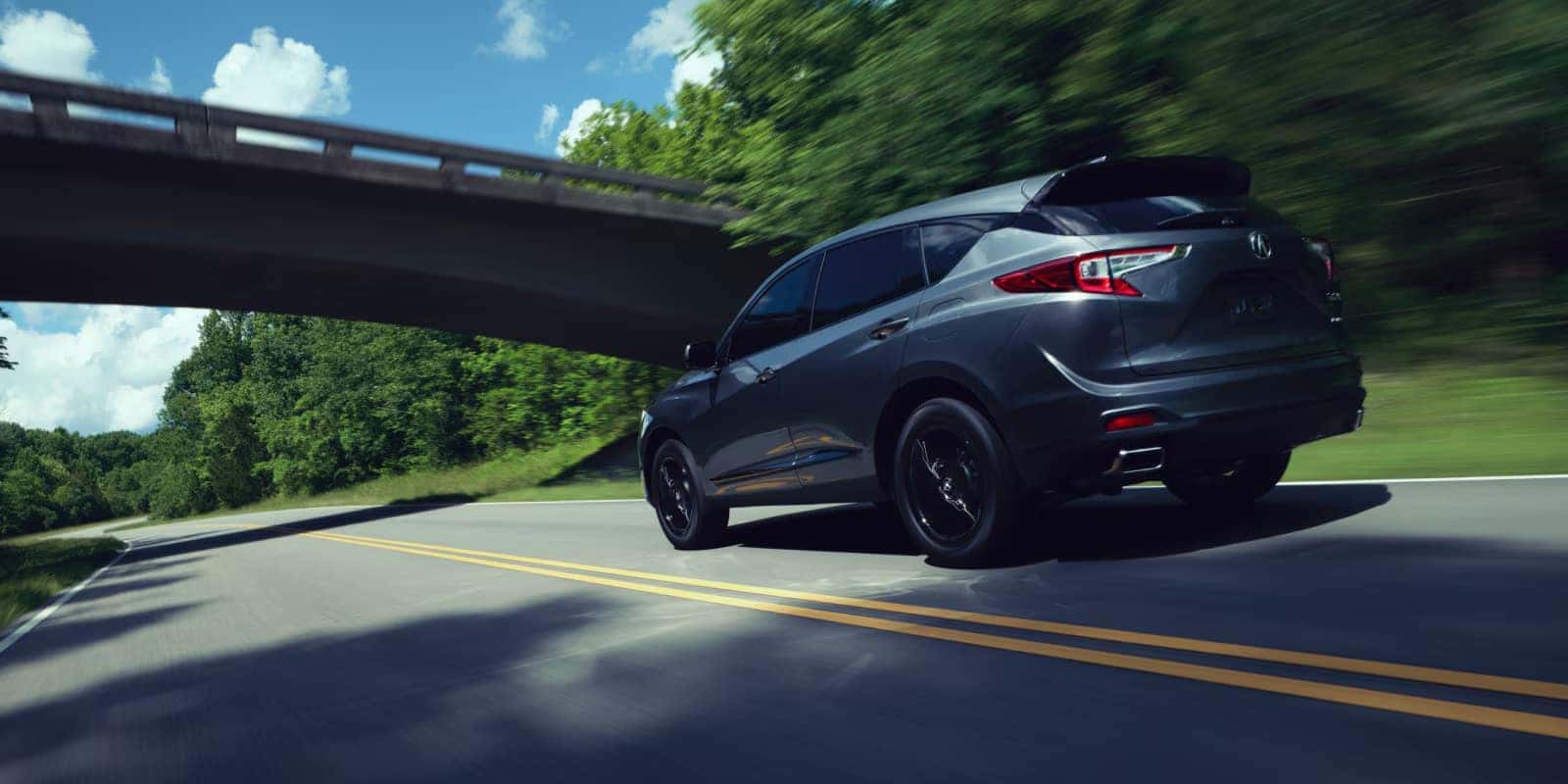 2026 Acura RDX driving under a bridge on a tree-lined road