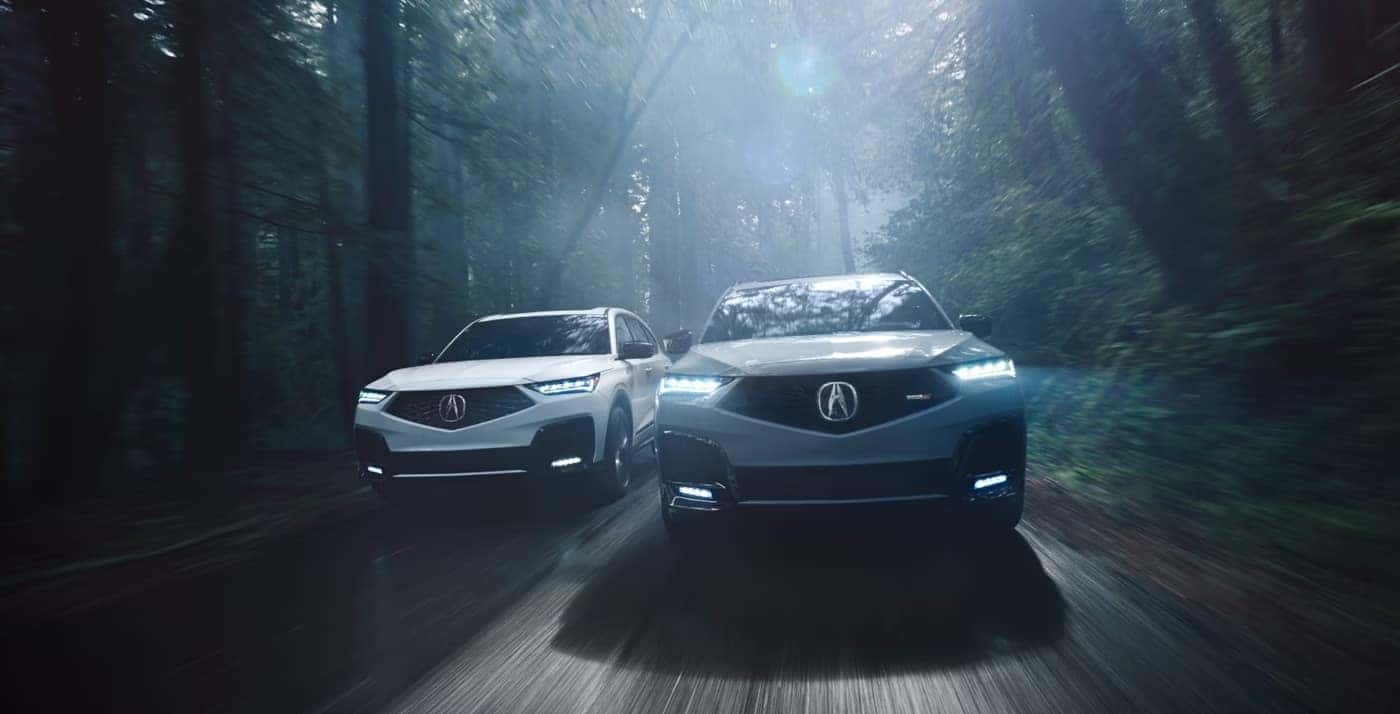 Two 2026 Acura MDX SUVs driving through a misty forest road
