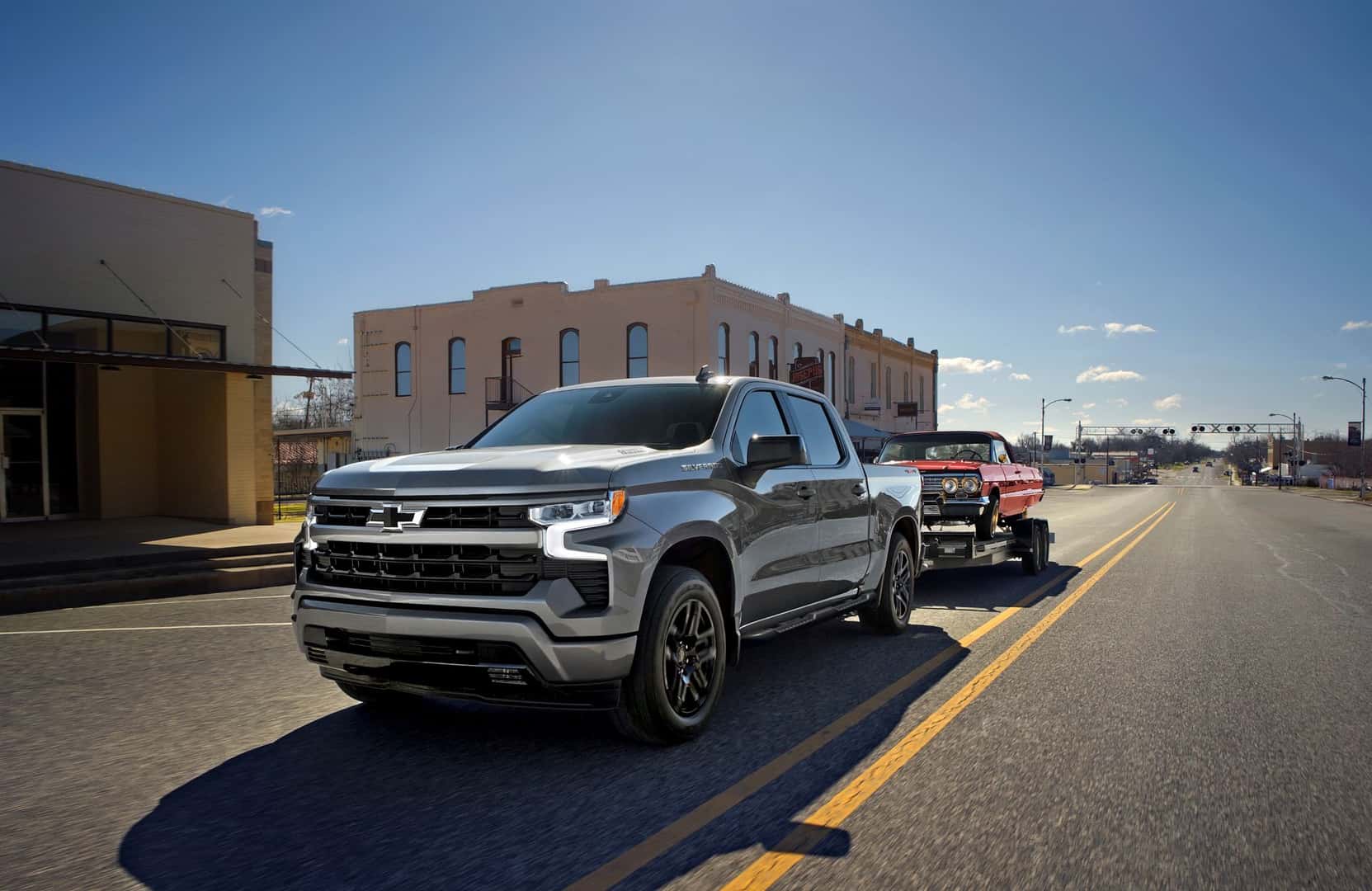 2026 Silverado 1500 towing a classic car in a rural town