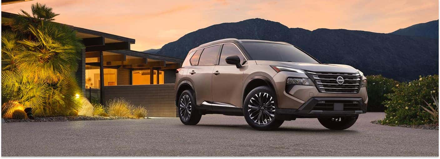 Champagne 2026 Nissan Rogue SUV parked in a residential driveway in front three-quarter view.