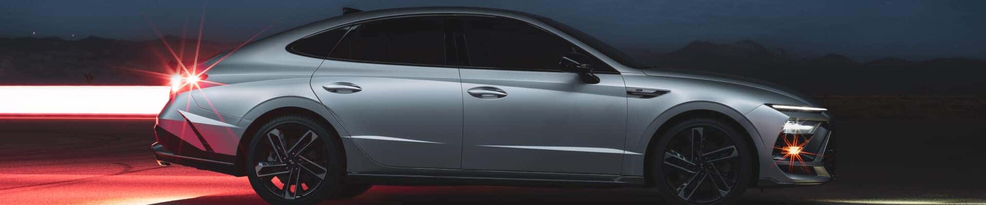 Side profile of a silver Hyundai Sonata parked on asphalt under a dark night sky.
