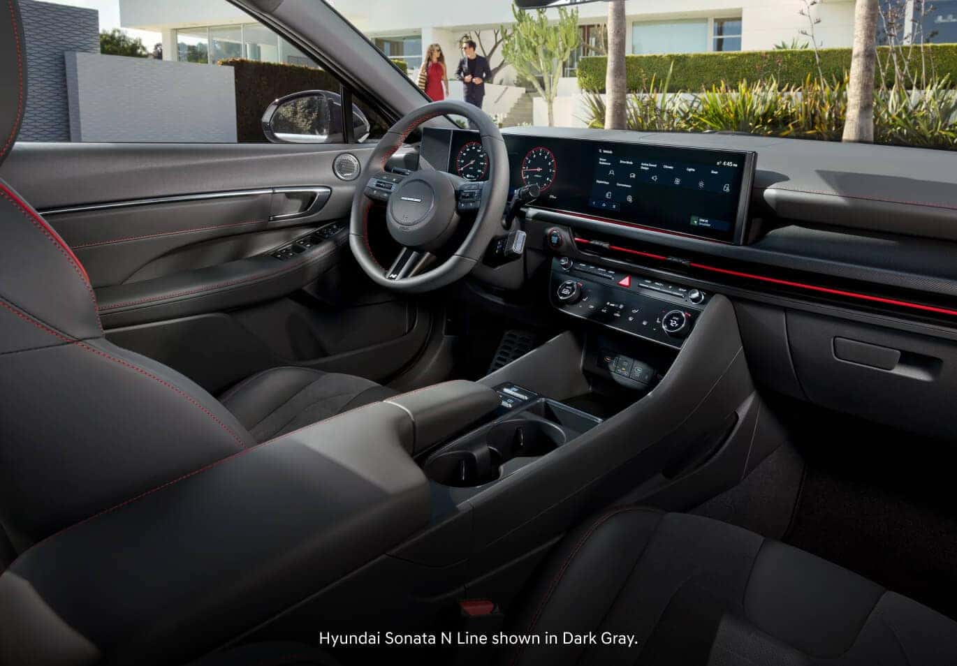 Interior dashboard view of a 2026 Hyundai Sonata N Line in Dark Gray featuring red stitching with a man and woman outside.