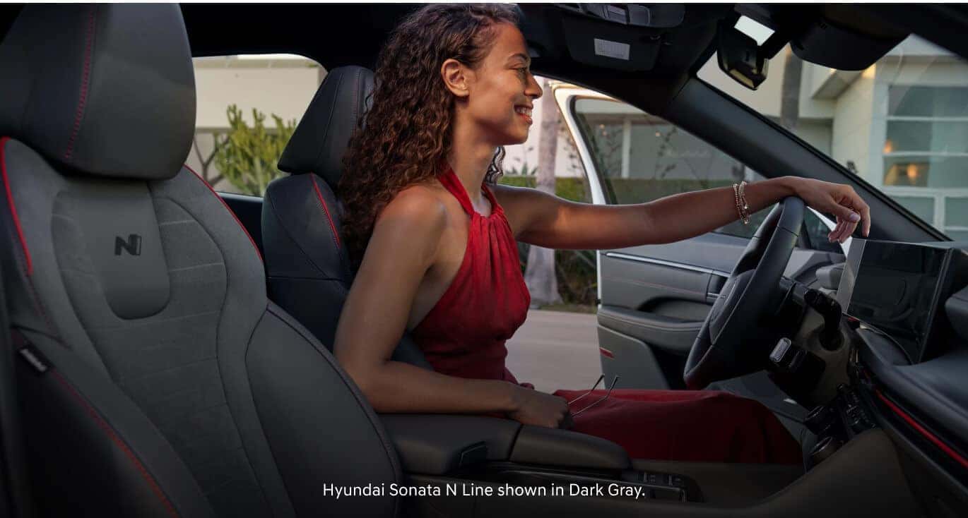 Interior view of a woman in a red halter dress sitting in the driver seat of a 2026 Hyundai Sonata N Line in Dark Gray.