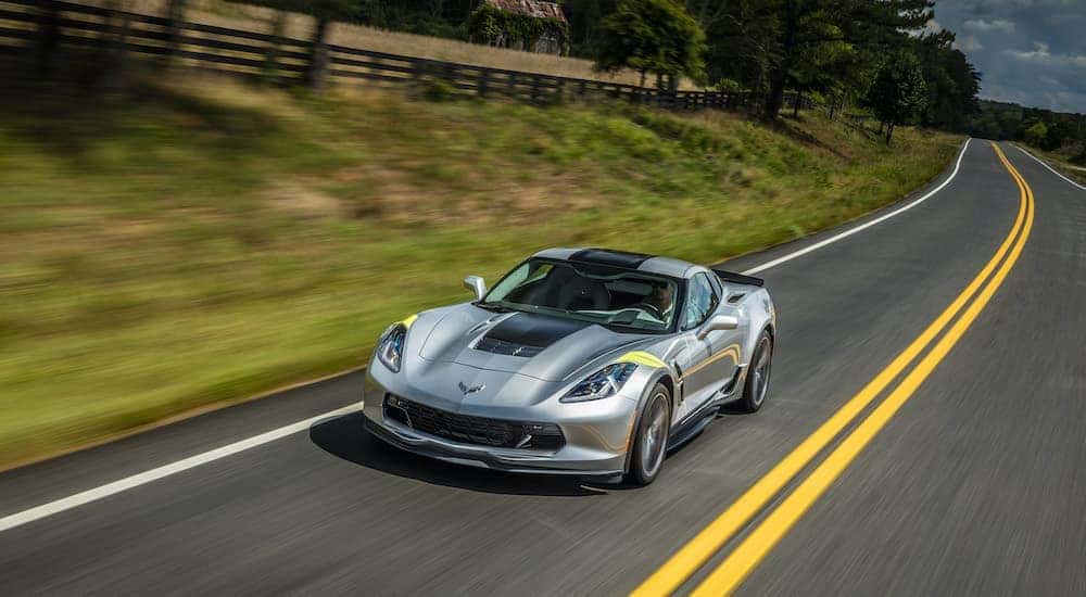 A grey 2018 Chevy Corvette is shown from the front driving on an open road lined with a fence.