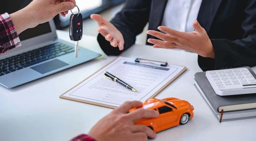 A person is shown holding car keys above a clipboard and toy car.