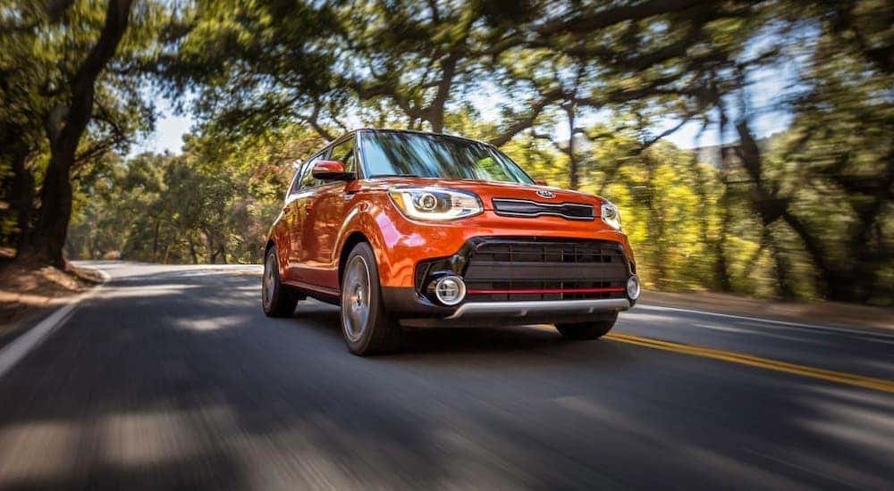 An orange 2019 Kia Soul is shown from the front driving down a two way road after leaving a used car dealership in Cincinnati.
