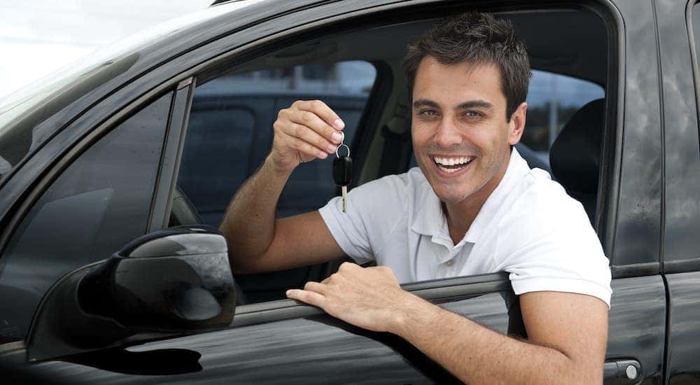 A smiling man is holding car keys in a black car.