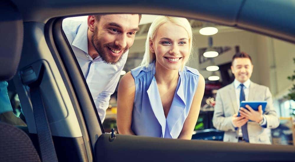 A couple is shown looking into a car at a dealership.