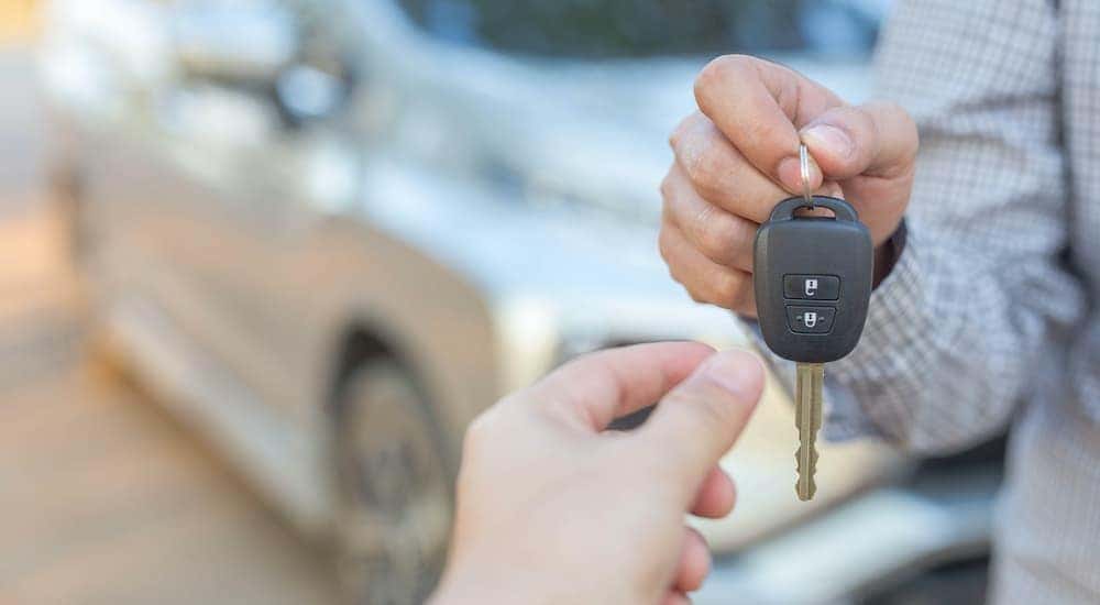 A person is shown passing a car key after searching "sell my car."
