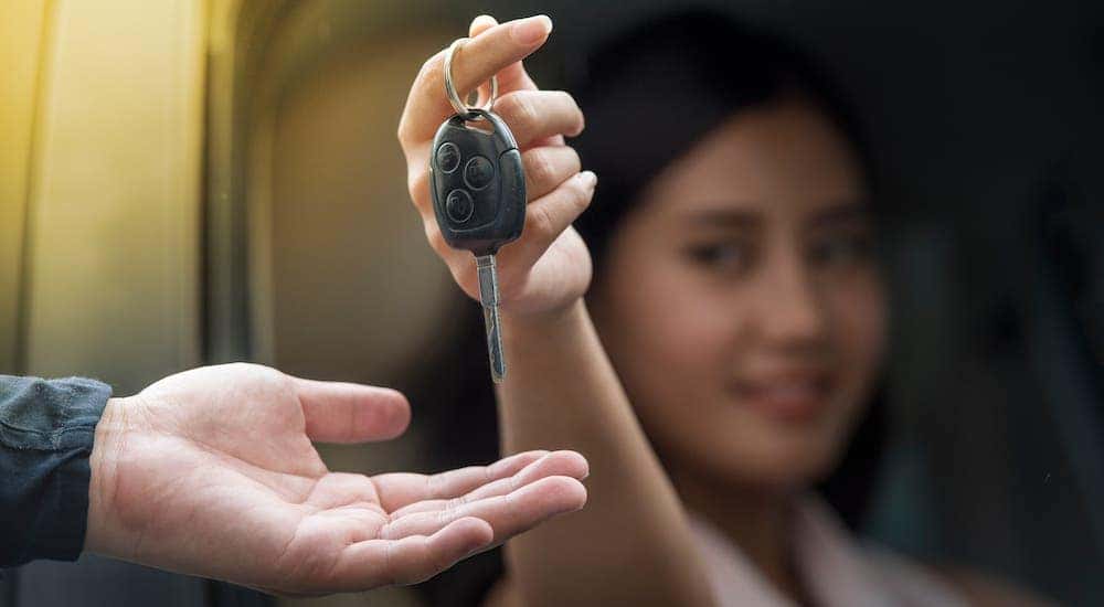 A woman is sitting inside a car and handing keys to a car dealer while selling her car fast.