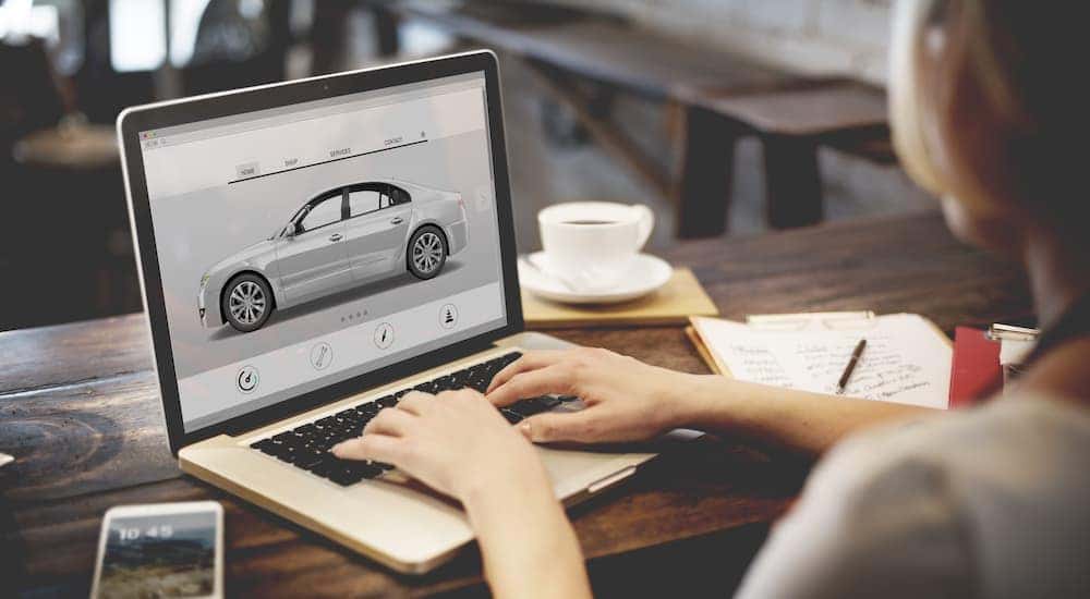 A person is shown typing on a laptop after searching 'sell my car.'