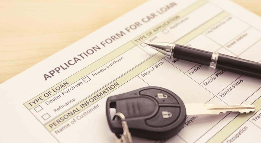 A close up shows a car key and pen on top of a car loan application.