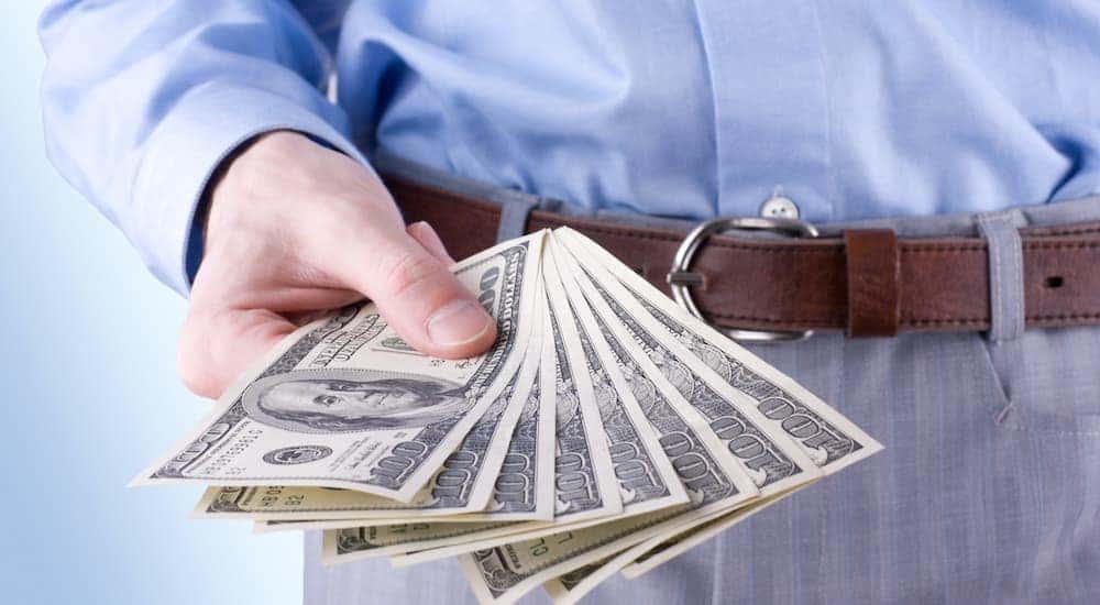 A person is shown holding a hand full of cash at a buy here pay here in Dayton.