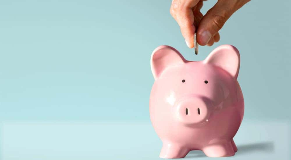 Hand putting a coin in the slot of a pink piggybank