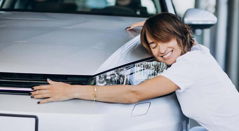 Woman in a white shirt with her arms around the front of a white vehicle