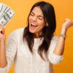 Woman in a white sweater holding up fanned-out cash against an orange background