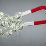 Hand holding a red and white horseshoe magnet with dollar bills coming toward it
