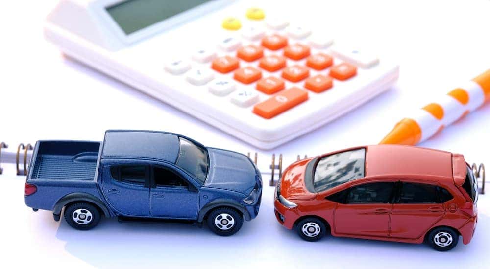 A blue toy trunk and a red toy van are shown facing each other on a desk with a calculator.