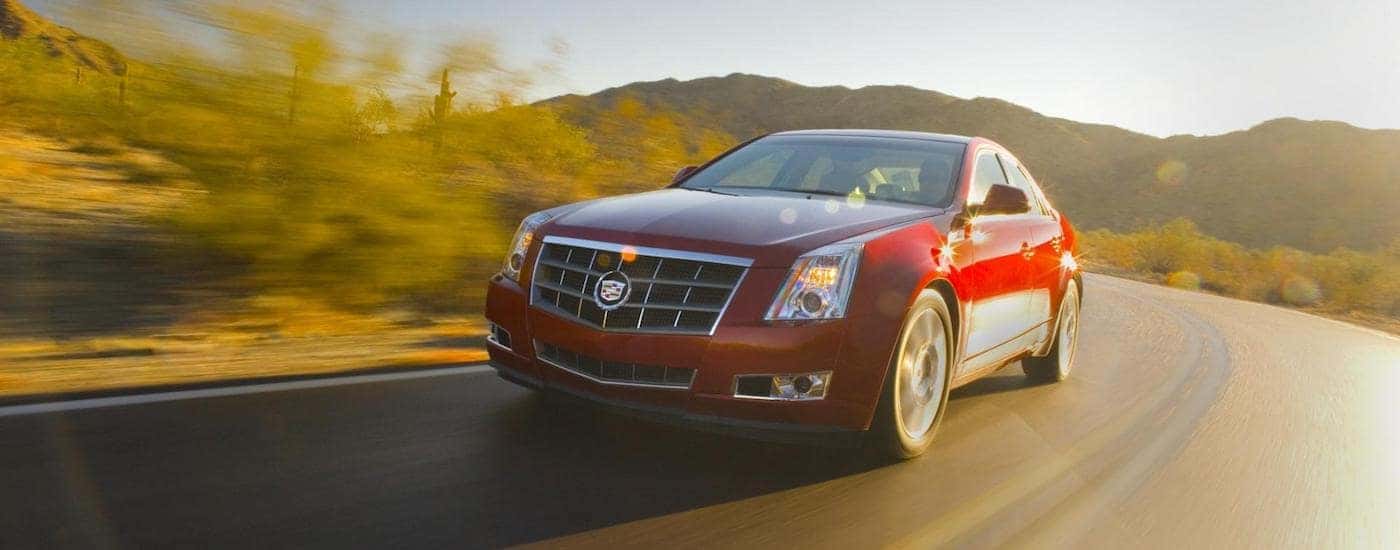 Red 2009 Used Cadillac CTS driving down a sunlit road in the mountains